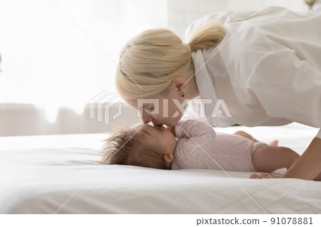Side view young loving beautiful mother kissing her cute baby Side view young loving beautiful mother kissing her cute baby 91078881