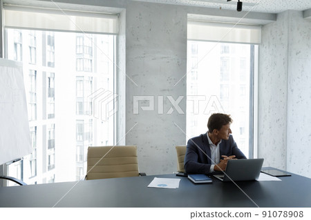 Successful businessman staring out window seated at modern skyscraper office 91078908