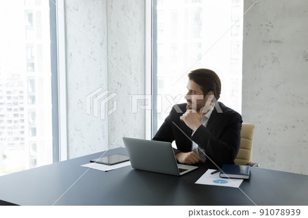 Businessman sit at desk with laptop staring aside looking thoughtful Businessman sit at desk with laptop staring aside looking thoughtful 91078939