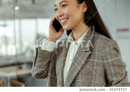 Close up of Asian business woman with a smile talking mobile phone at the office 91079737