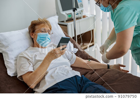 Sick senior patient use phone during medical procedure in hospital ward Sick senior patient use phone during medical procedure in hospital ward 91079750