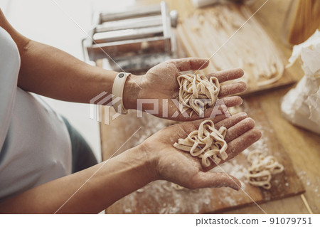 A woman in her kitchen holds in her palms the homemade noodles she has just cooked. A woman in her kitchen holds in her palms the homemade noodles she has just cooked. 91079751