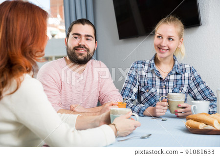 Smiling woman with cup of tea talking with adult children 91081633