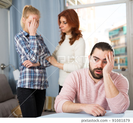 Angry wife and mother-in-law rebuking young man 91081879