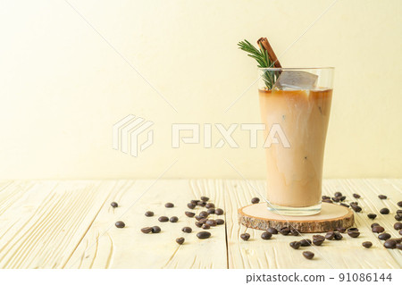pouring milk in black coffee glass with ice cube, cinnamon and rosemary pouring milk in black coffee glass with ice cube, cinnamon and rosemary 91086144