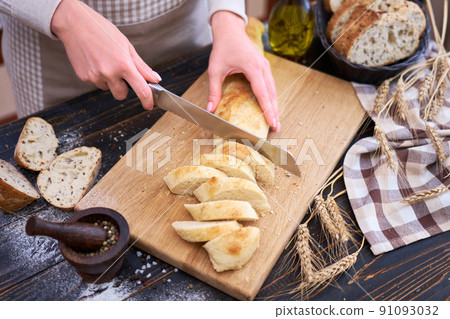 Woman cutting freshly baked bread at wooden kitchen table Woman cutting freshly baked bread at wooden kitchen table 91093032