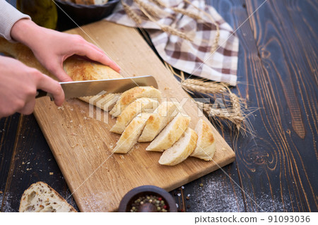 Woman cutting freshly baked bread at wooden kitchen table 91093036