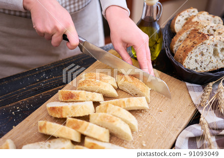 Woman cutting freshly baked bread at wooden kitchen table Woman cutting freshly baked bread at wooden kitchen table 91093049