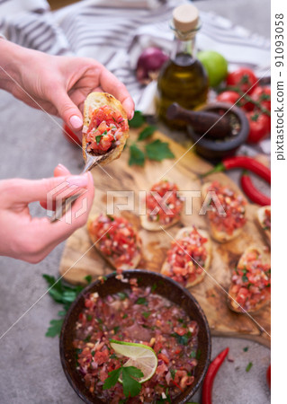 Woman making tasty salsa bruschetta snacks at domestic kitchen Woman making tasty salsa bruschetta snacks at domestic kitchen 91093058