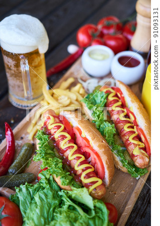 BBQ hot dog served with vegetables and French fries and sauces on wooden serving board 91093131