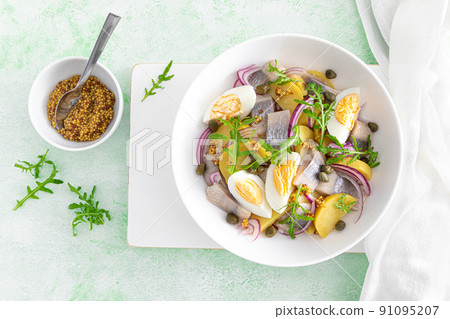 Herring and boiled potato salad with egg, capers and red onion. Top view 91095207