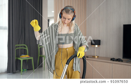 Young girl havig fun while cleaning floor with vacuum cleaner. Happy woman doing housework at home enjoy music wearing earphones. 91097650