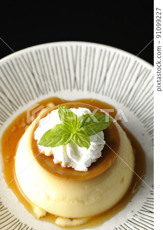 A bird's-eye view of the old-fashioned retro pudding with mint leaves and fresh cream served on a flat plate on a black background. 91099227