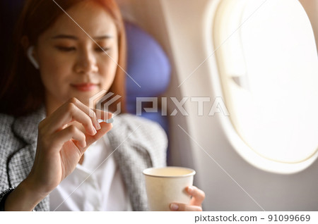 Asian female passenger feeling dizzy, taking an airsick motion sickness pills before take off 91099669