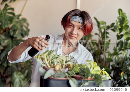 Happy Asian guy taking care of plants and holding spray bottle Happy Asian guy taking care of plants and holding spray bottle 91099946