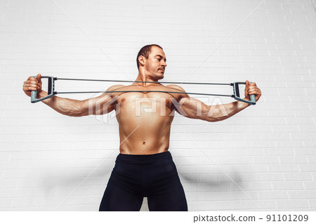 Handsome young sportsman exercising using expander while standing against white background Handsome young sportsman exercising using expander while standing against white background 91101209