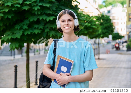 Smiling teenage male student with textbooks looking at camera outdoor 91101220