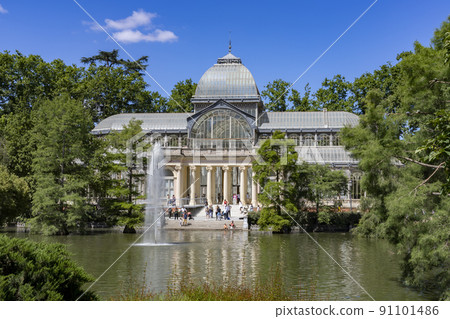 Crystal Palace. Building located in the Retiro Park in Madrid with its glass windows surrounded by trees and green vegetation on a sunny day and some clouds in the sky, in Spain. Europe. Photography. 91101486