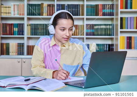High school student girl in headphones studying in school library using books and laptop High school student girl in headphones studying in school library using books and laptop 91101501