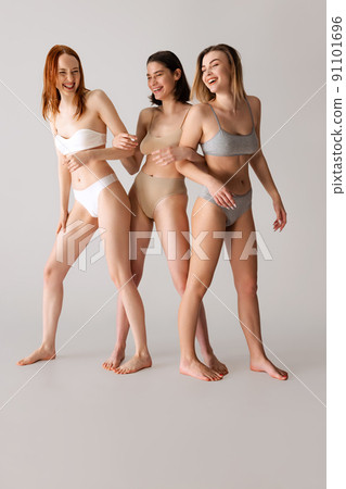 Portrait of three beautiful cheerful women posing in underwear isolated over grey studio background. Happy youth. Portrait of three beautiful cheerful women posing in underwear isolated over grey studio background. Happy youth. 91101696