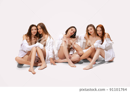 Group of young beautiful women posing in beige cotton underwear and shirt, sitting isolated over white studio background 91101764