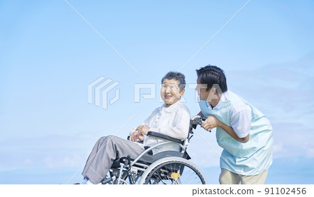 Elderly woman going outdoors with a nurse in a wheelchair 91102456