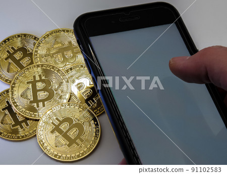 Bitcoin coins in golden metal with a man's hand beside him holding a smarthphone Bitcoin coins in golden metal with a man's hand beside him holding a smarthphone 91102583