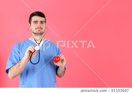 Nurse man holds red heart on pink background Nurse man holds red heart on pink background 91103687