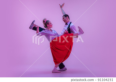 Stylish young man and pretty woman in vintage style outfits dancing retro dance isolated on very peri color background in neon light. 91104231