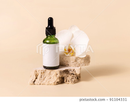Green dropper glass bottle near white orchid flower on light yellow, Mockup. Skincare product 91104331