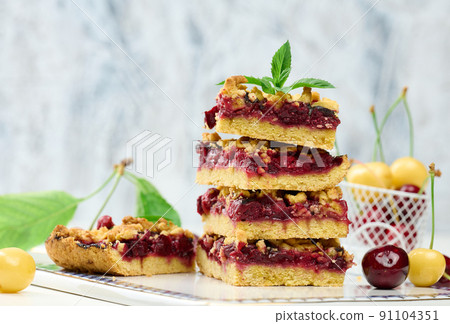 Square slices of cherry crumble lie in a stack on a white board 91104351