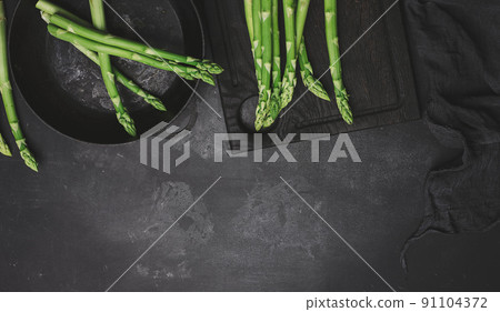 Fresh green asparagus in a round cast iron pan on a black table Fresh green asparagus in a round cast iron pan on a black table 91104372