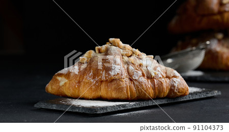 Baked croissant on a wooden board and sprinkled with powdered sugar, black table. Appetizing pastries for breakfast 91104373
