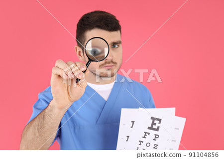 Male nurse holds magnifier and vision test on pink background Male nurse holds magnifier and vision test on pink background 91104856