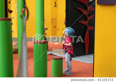 Child climbing on wall in amusement centre. Climbing training for children. Little girl in dressed climbing gear climb high. Extreme active leisure for kids. 91105153
