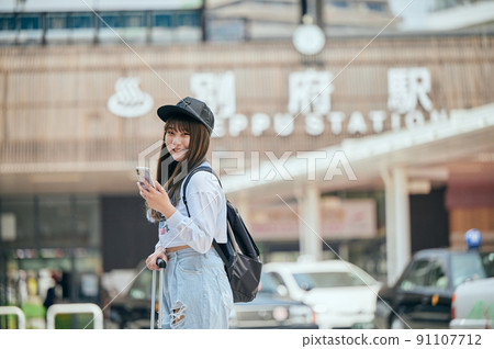 A young woman sightseeing with a smartphone in front of Beppu Station 91107712