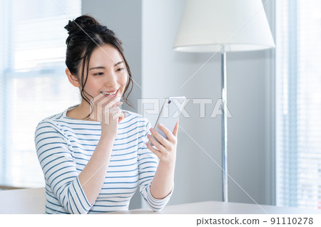 一個年輕的女人，在客廳裡操作智能手機 91110278