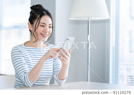 一個年輕的女人,在客廳裡操作智能手機 一個年輕的女人,在客廳裡操作智能手機 91110279