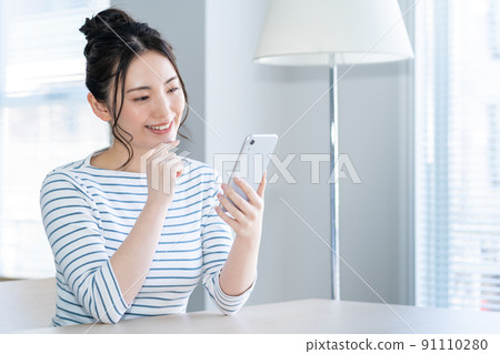 一個年輕的女人,在客廳裡操作智能手機 一個年輕的女人,在客廳裡操作智能手機 91110280