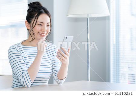 一個年輕的女人,在客廳裡操作智能手機 一個年輕的女人,在客廳裡操作智能手機 91110281