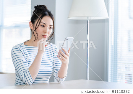 一個年輕的女人,在客廳裡操作智能手機 一個年輕的女人,在客廳裡操作智能手機 91110282