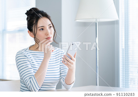 一個年輕的女人,在客廳裡操作智能手機 一個年輕的女人,在客廳裡操作智能手機 91110283