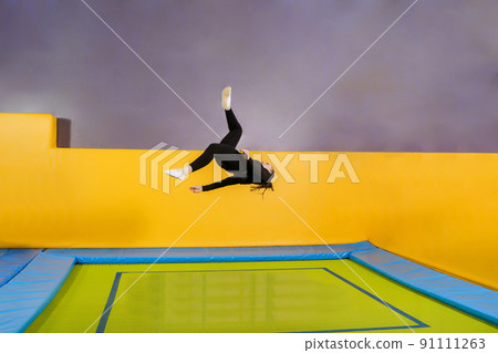 Young woman amateur acrobatic athlete jumping and exercising on a trampoline indoors, modern hobby and fitness concept 91111263