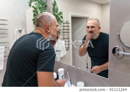 Man shaving with razor using foam in bathroom in the morning 91111264