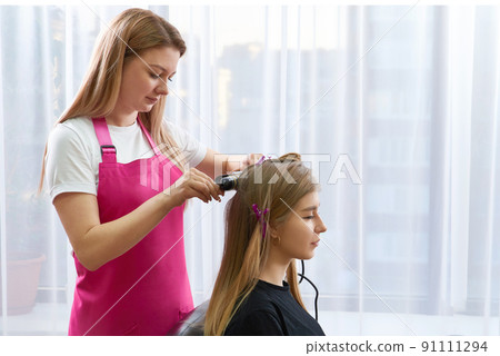 Hairdresser makes hairstyle girl with long hair in a beauty salon. Create curls with curling irons 91111294
