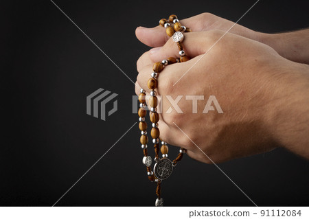 Folded hands of a young man holding a rosary during a pray isolated on black background 91112084