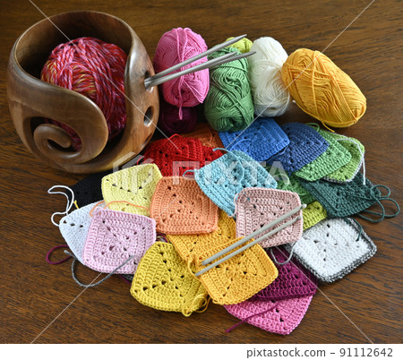 colorful knitted squares, skeins of wool and a wooden yarn bowl 91112642