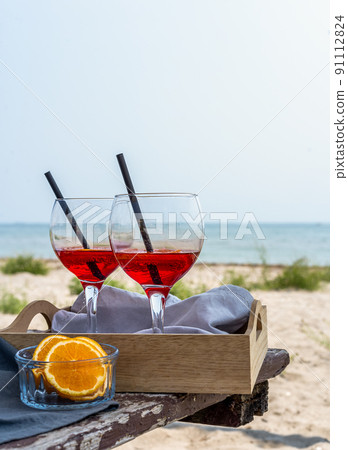 Two glasses of an Italian appetiser Gingerino drink in tray on old table, on the beach with sea coast view 91112824