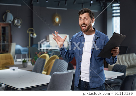 Excited salesman screaming proud, celebrating success with raised hands in furniture store. Portrait of happy caucasian man in denim shirt feeling joy, while standing in showroom. Concept of emotions. Excited salesman screaming proud, celebrating success with raised hands in furniture store. Portrait of happy caucasian man in denim shirt feeling joy, while standing in showroom. Concept of emotions. 91113189