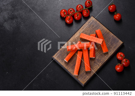 Crab sticks on a cutting Board with a knife. On black concrete background 91113442